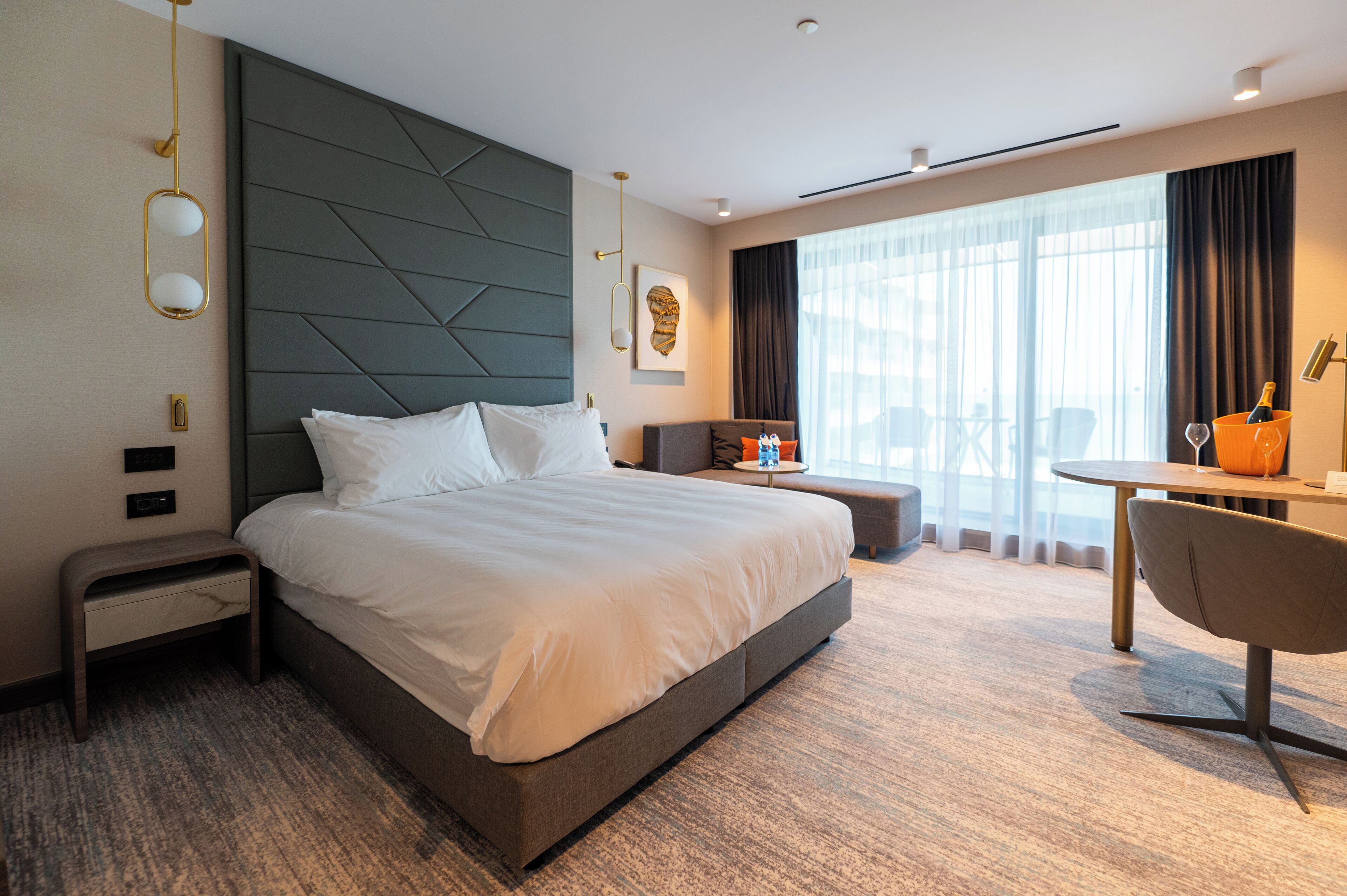 A modern hotel room with a large bed, a desk, and a chair.