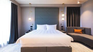 A modern hotel room with a large bed, a sofa, and a headboard with a geometric pattern.