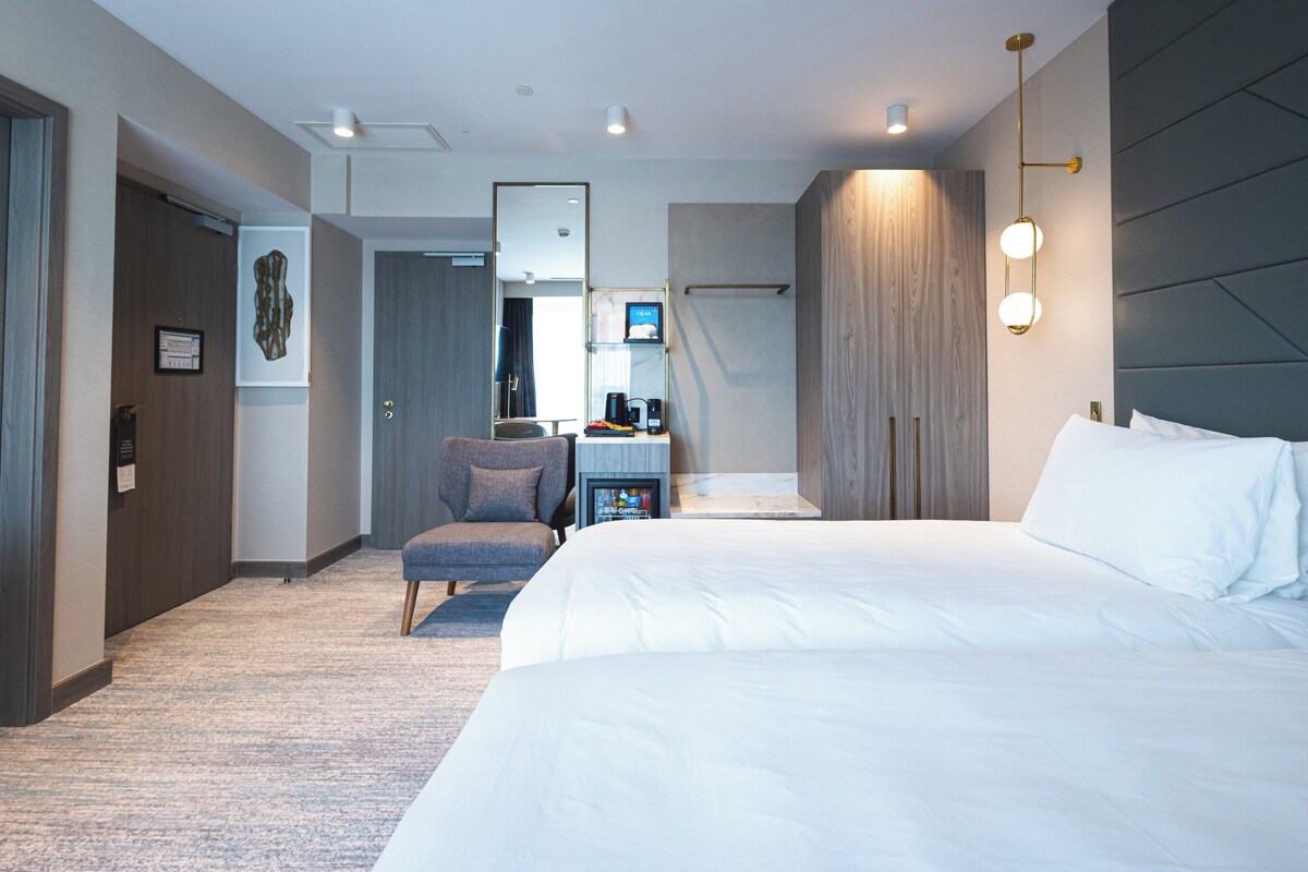 Ein modernes Hotelzimmer mit einem großen Bett, einem Schreibtisch mit Computer, einem Stuhl und einem Kleiderschrank.