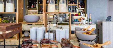 A breakfast buffet with jars of jam, plates, and a bowl of cereal.