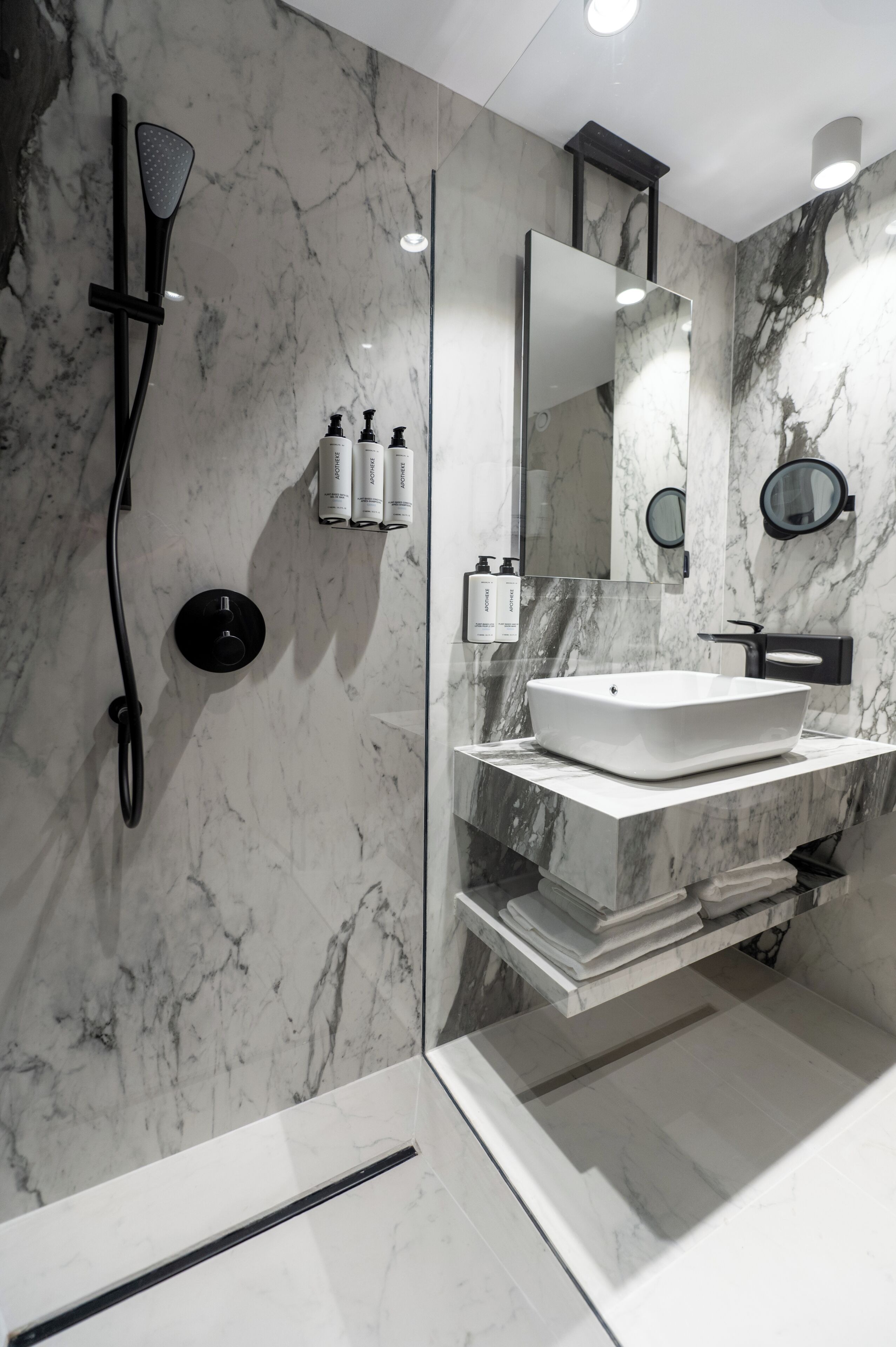 Un baño moderno con un espejo grande, un lavamanos blanco y una ducha con cabezal de ducha de mano.