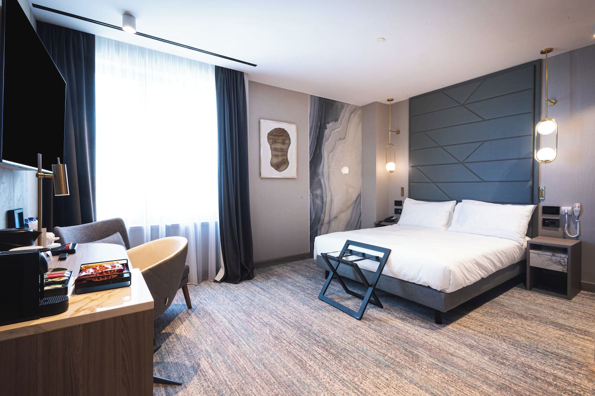 Ein modernes Hotelzimmer mit Bett, Schreibtisch, Stuhl und einem großen Fenster mit Vorhängen.