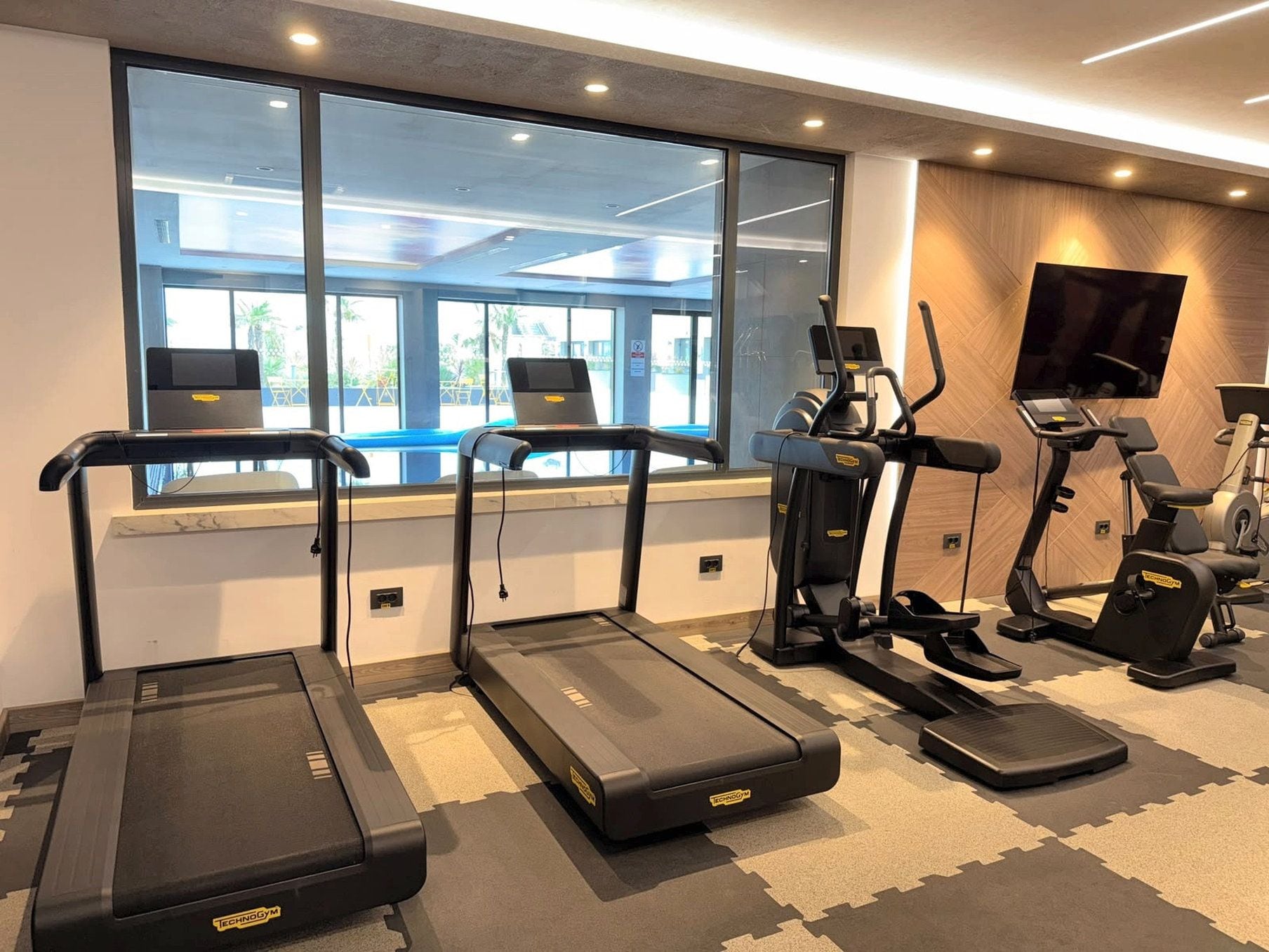 A gym with treadmills, elliptical machines, and a television screen.