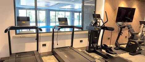 A gym with treadmills, elliptical machines, and a television screen.