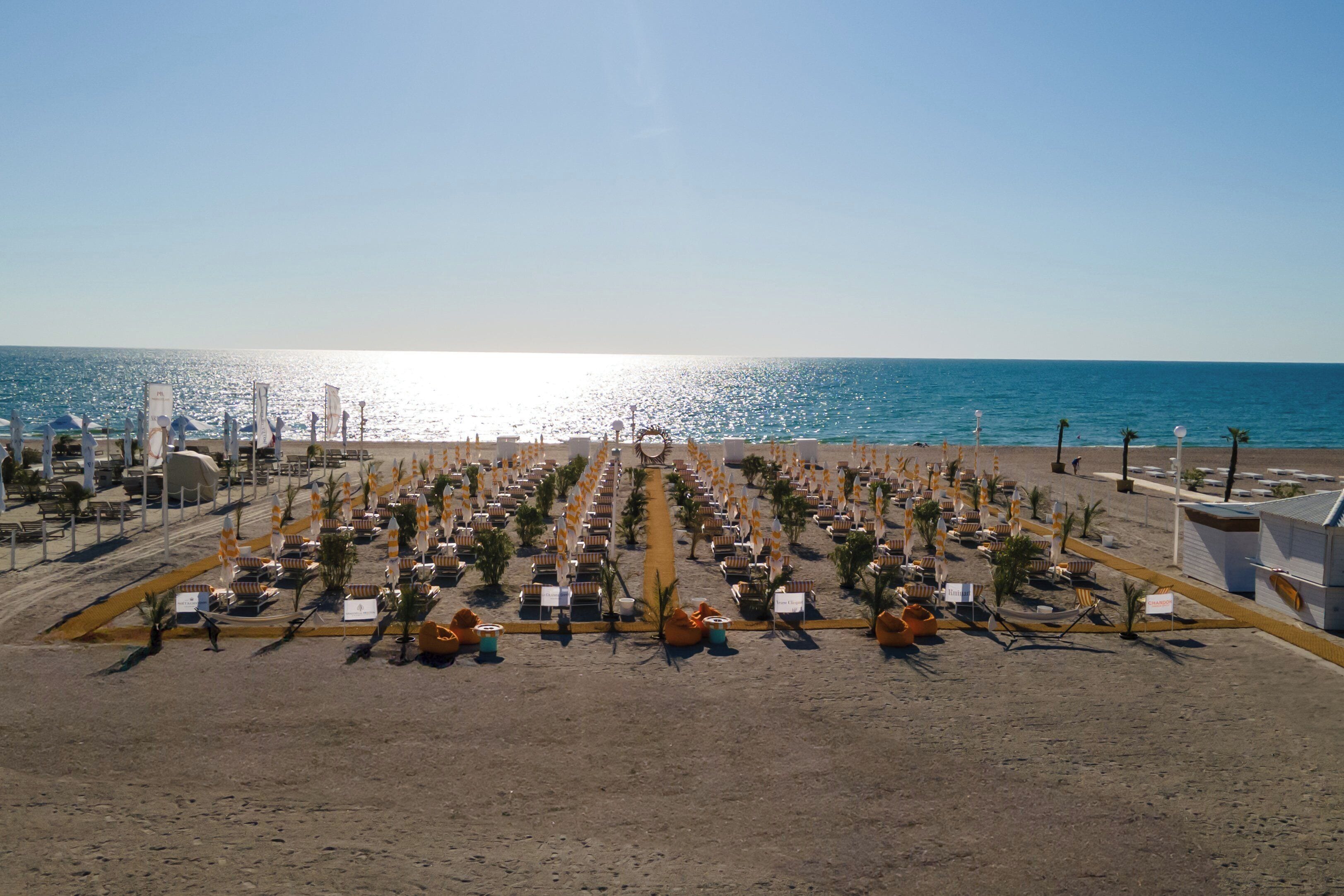 Un complexe hôtelier de bord de mer avec des rangées de chaises longues et de parasols, une vue dégagée sur l’océan et une plage de sable.