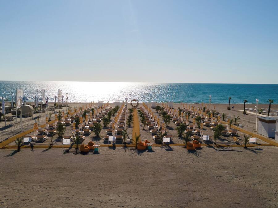 A beach resort with rows of sun loungers and umbrellas, a clear view of the ocean, and a sandy beach.