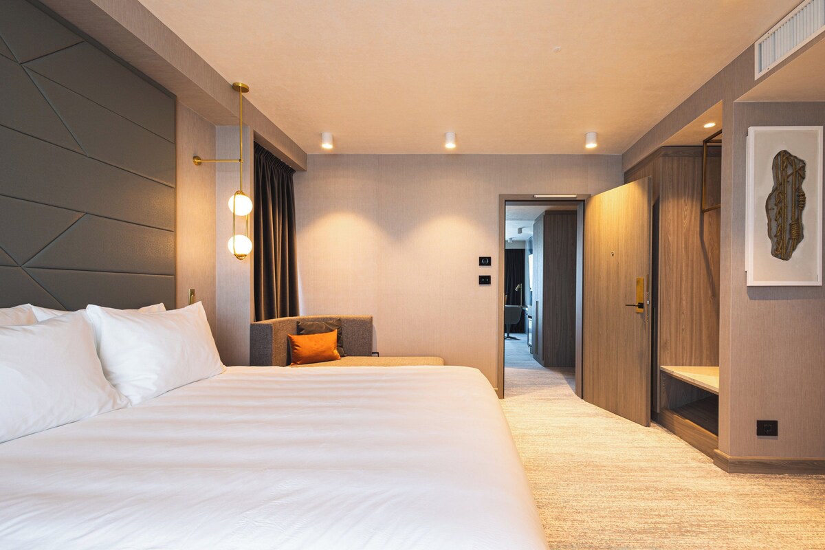 Ein modernes Hotelzimmer mit einem großen Bett, einem Schreibtisch und einem begehbaren Kleiderschrank.