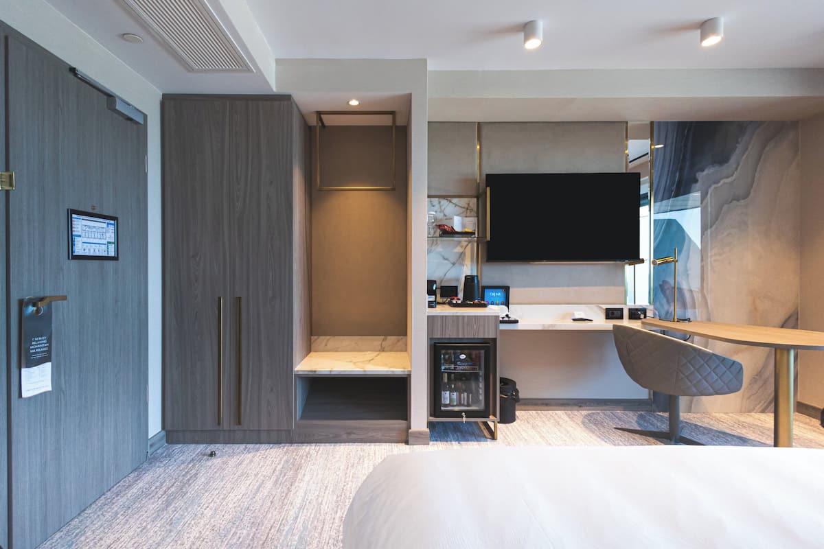 Ein modernes Hotelzimmer mit einem Bett, einem Schreibtisch mit Computer, einem Flachbildfernseher und einer Sitzecke mit gepolstertem Sessel.