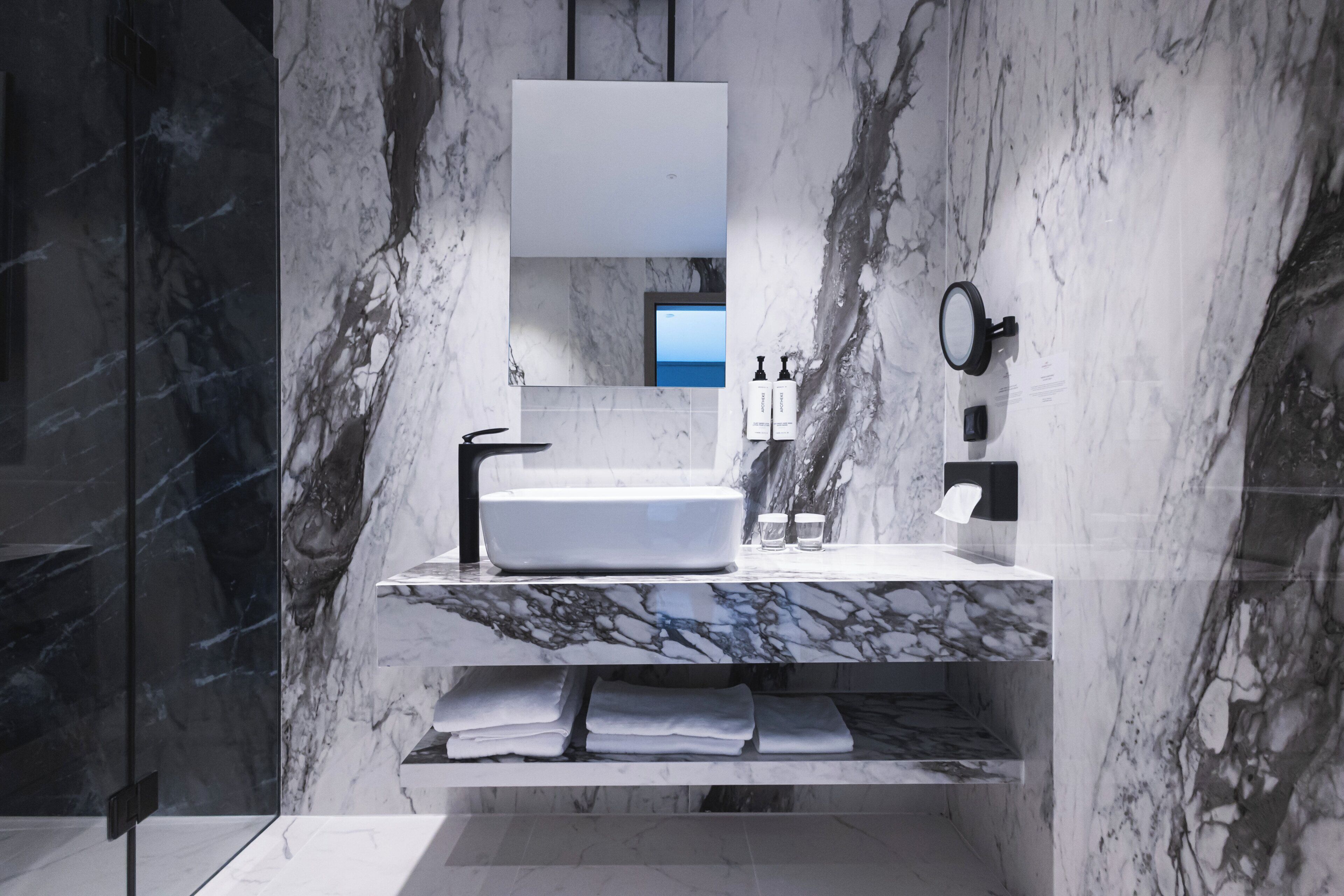 A modern bathroom with a marble sink, a large mirror, and a built-in shelf with towels.