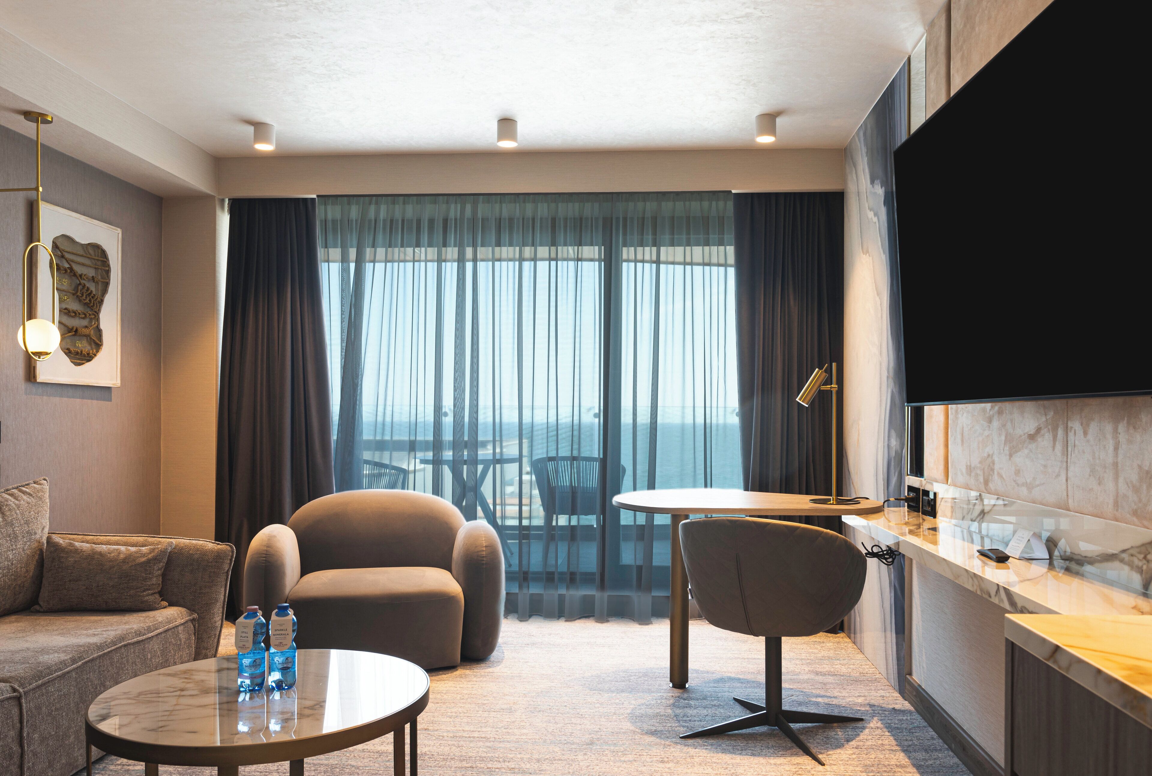 Habitación de hotel con sofá, dos sillones, una mesita, televisor y balcón con vistas.