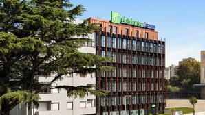 A modern building with a Holiday Inn Express sign, featuring a glass facade and a mix of red and brown exterior panels. - Holiday Inn Express Porto Boavista by IHG (Porto)
