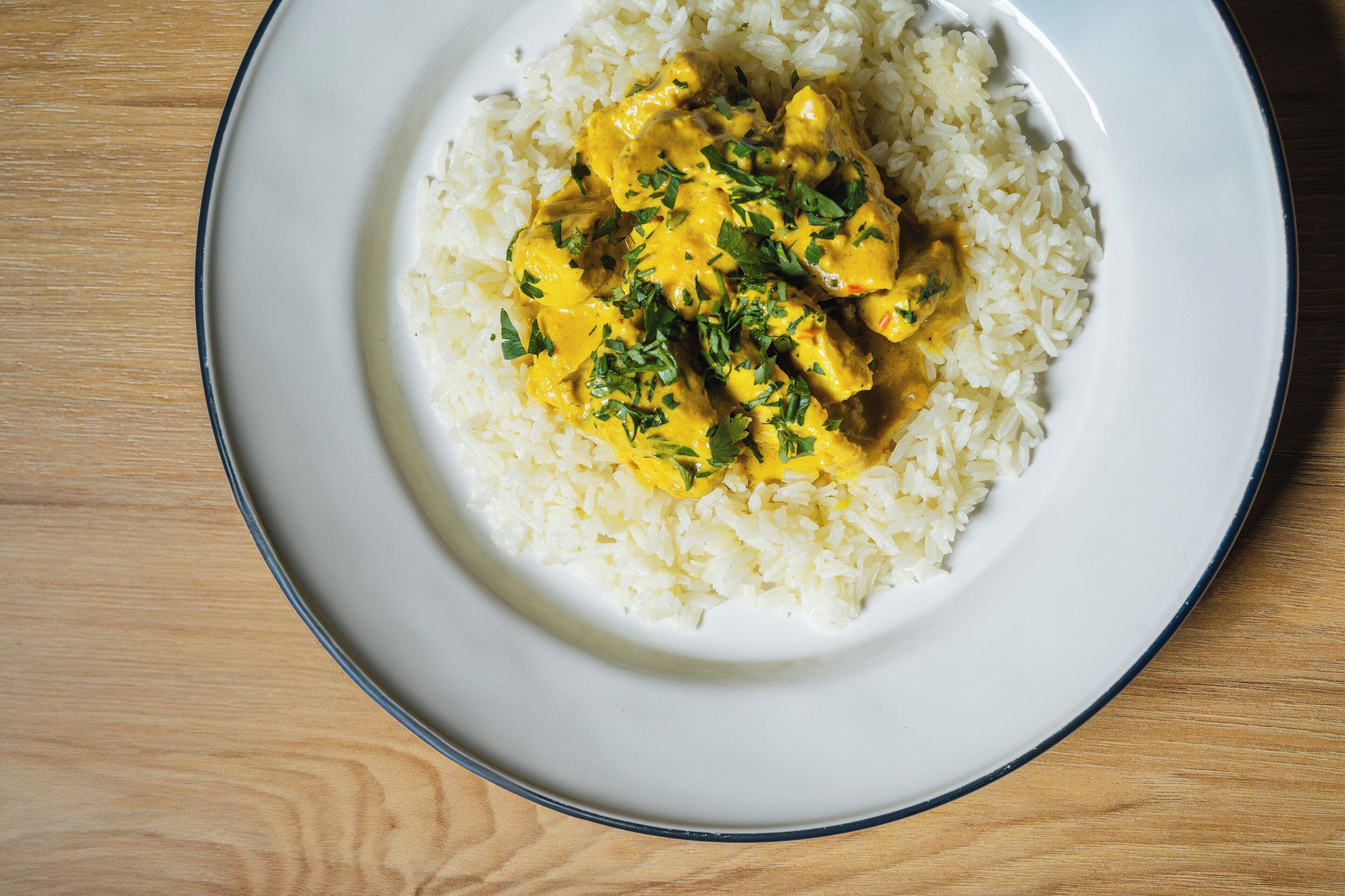 Un plato de arroz blanco con curry amarillo y hierbas verdes sobre una mesa de madera.