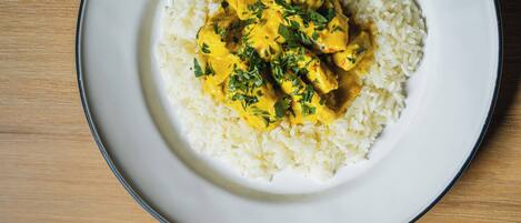 A plate of white rice with yellow curry and green herbs on a wooden table.