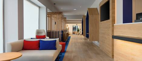 A modern hotel lobby with a sofa, ottoman, and a reception desk.