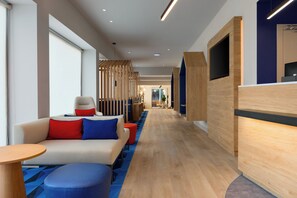 Een moderne hotel lobby met een bank, poef en een receptiebalie.