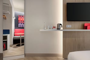 Habitación de hotel moderna con cama, una mesita pequeña con un hervidor, tazas y una botella.