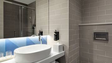 A modern bathroom with a large white sink, a glass shower enclosure, and a towel rack.