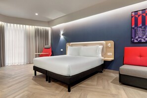 Een moderne hotelkamer met een groot bed, een rode fauteuil, een grijze bank en een televisie aan de muur.
