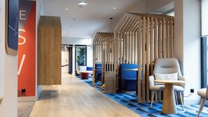 A modern interior with a wooden reception desk, blue and beige seating, and a patterned floor. - Holiday Inn Express Porto Boavista by IHG (Porto)