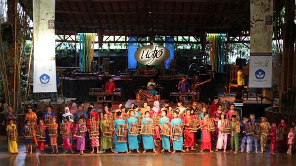 A group of people in traditional costumes on a stage with musical instruments and a banner reading "Udo". - Hotel Indigo Bandung Dago Pakar by IHG (Bandung)