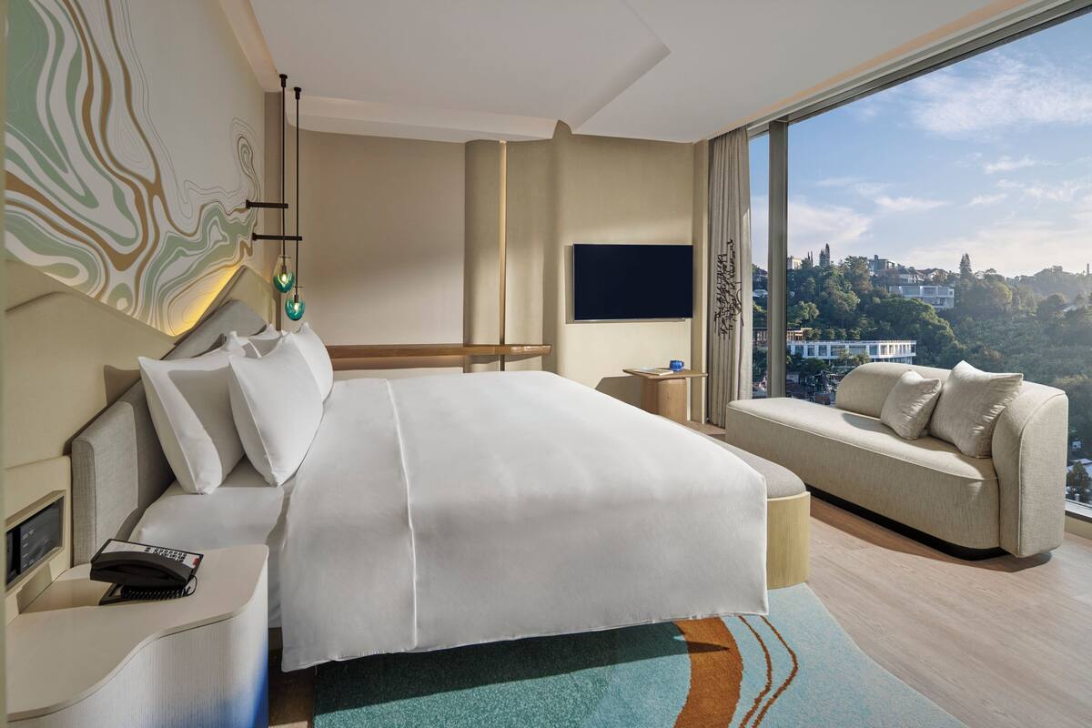 Ett modernt hotellrum med en stor säng, en soffa, en TV och utsikt över staden.