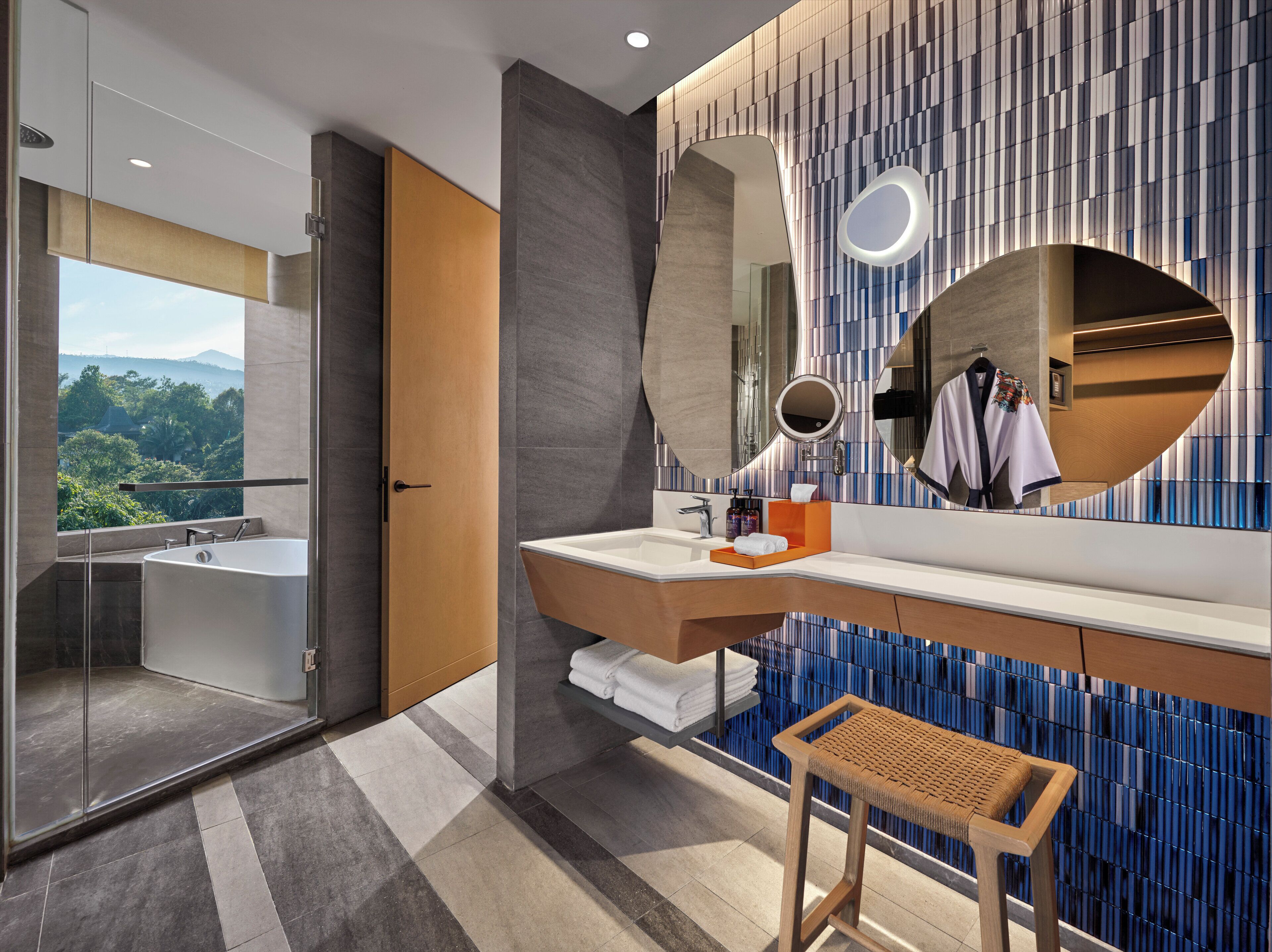 Une salle de bain moderne avec une grande baignoire, un meuble-lavabo avec un miroir et une vue sur l’extérieur.