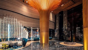 Un hall d’entrée moderne avec une colonne centrale en bois, un espace salon et un mur décoratif.