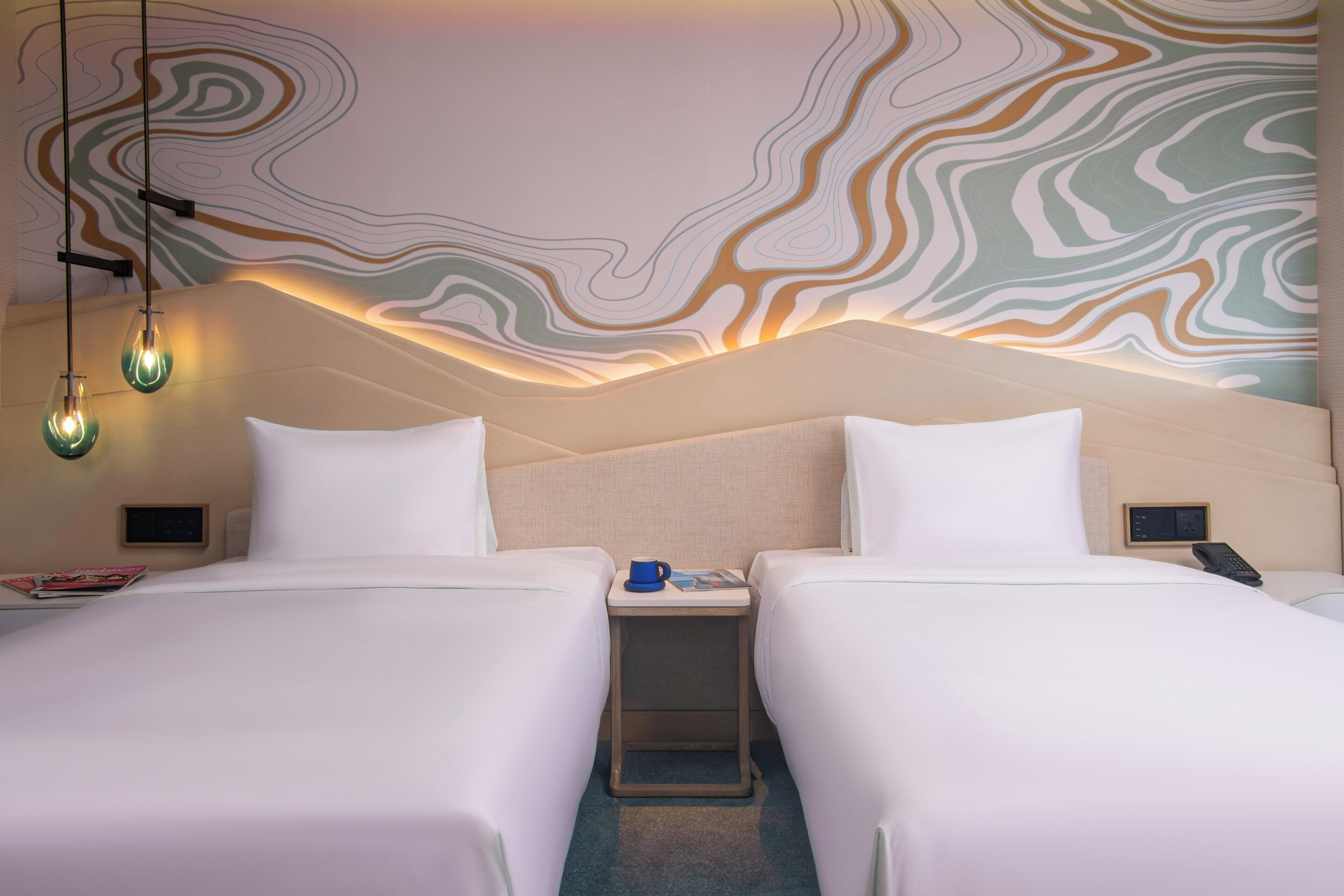 A hotel room with two beds, a nightstand with a lamp, and a wall with a wavy pattern.