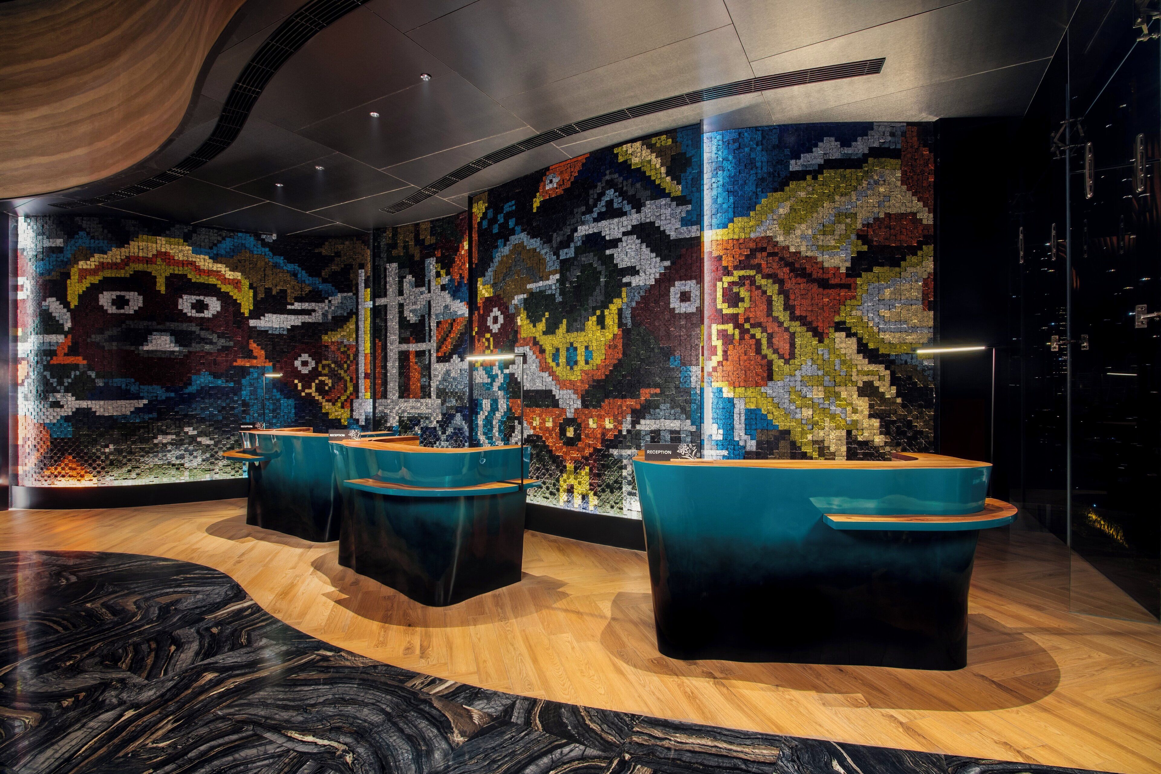 A lobby with a colorful mosaic wall, wooden flooring, and modern reception desks.
