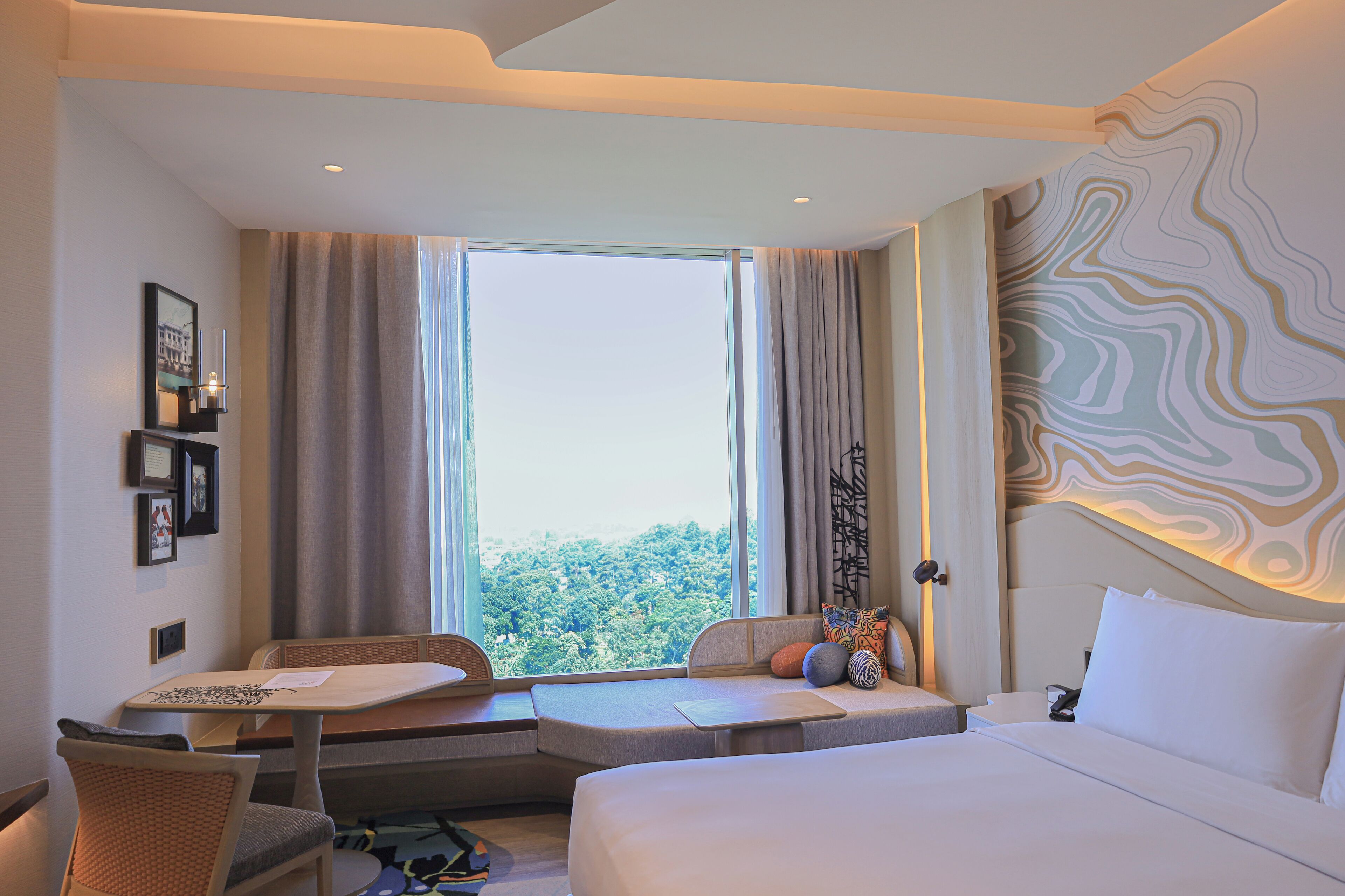 A hotel room with a large window, a bed, a seating area, and a desk.