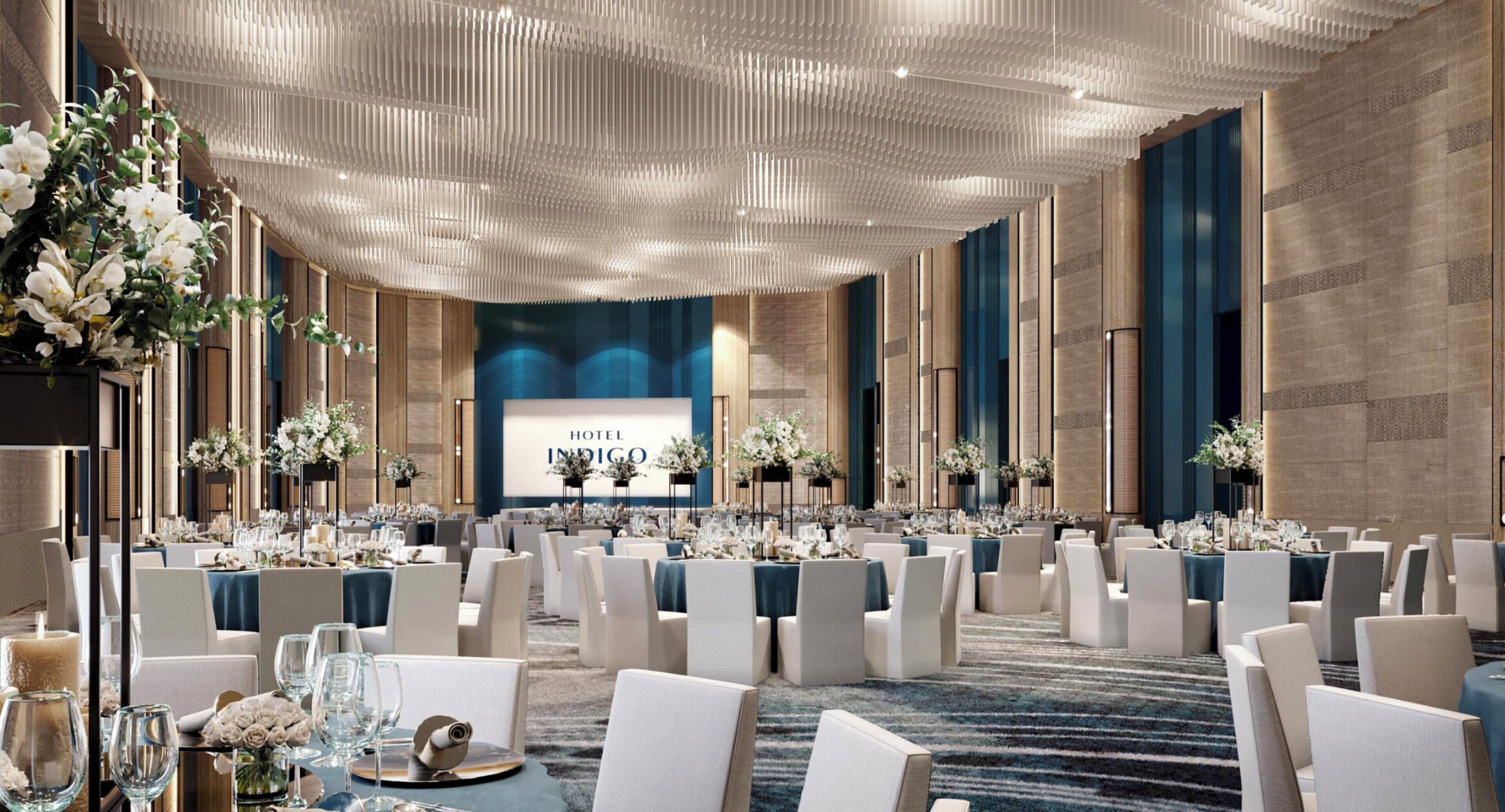 Une salle de conférence d’hôtel avec des rangées de tables, de chaises et des centres de table ornés de compositions florales.