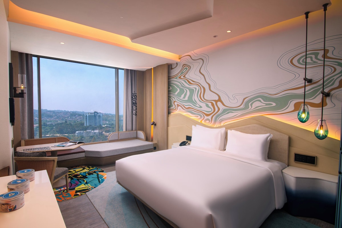 Ein modernes Hotelzimmer mit einem großen Bett, einer Sitzecke mit Blick und einer Wand mit abstraktem Design.