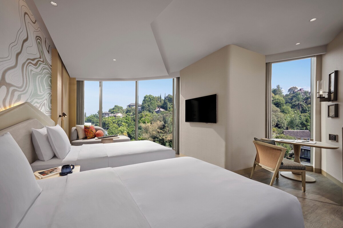 Une chambre d’hôtel moderne, dotée de deux lits, d’un bureau et d’une grande fenêtre donnant sur le paysage environnant.