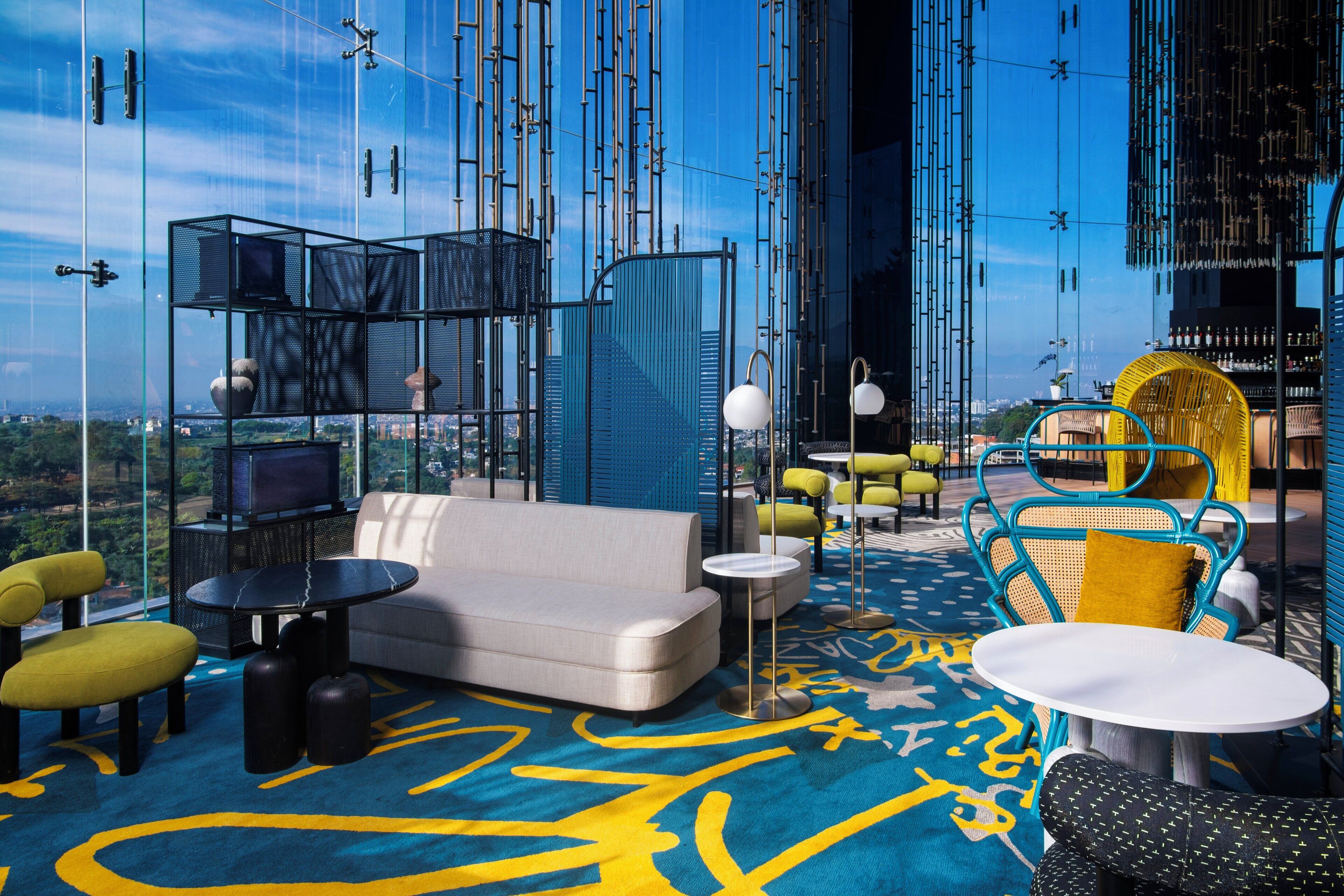 A modern lounge with a sofa, chairs, and tables, featuring a city view through large windows.