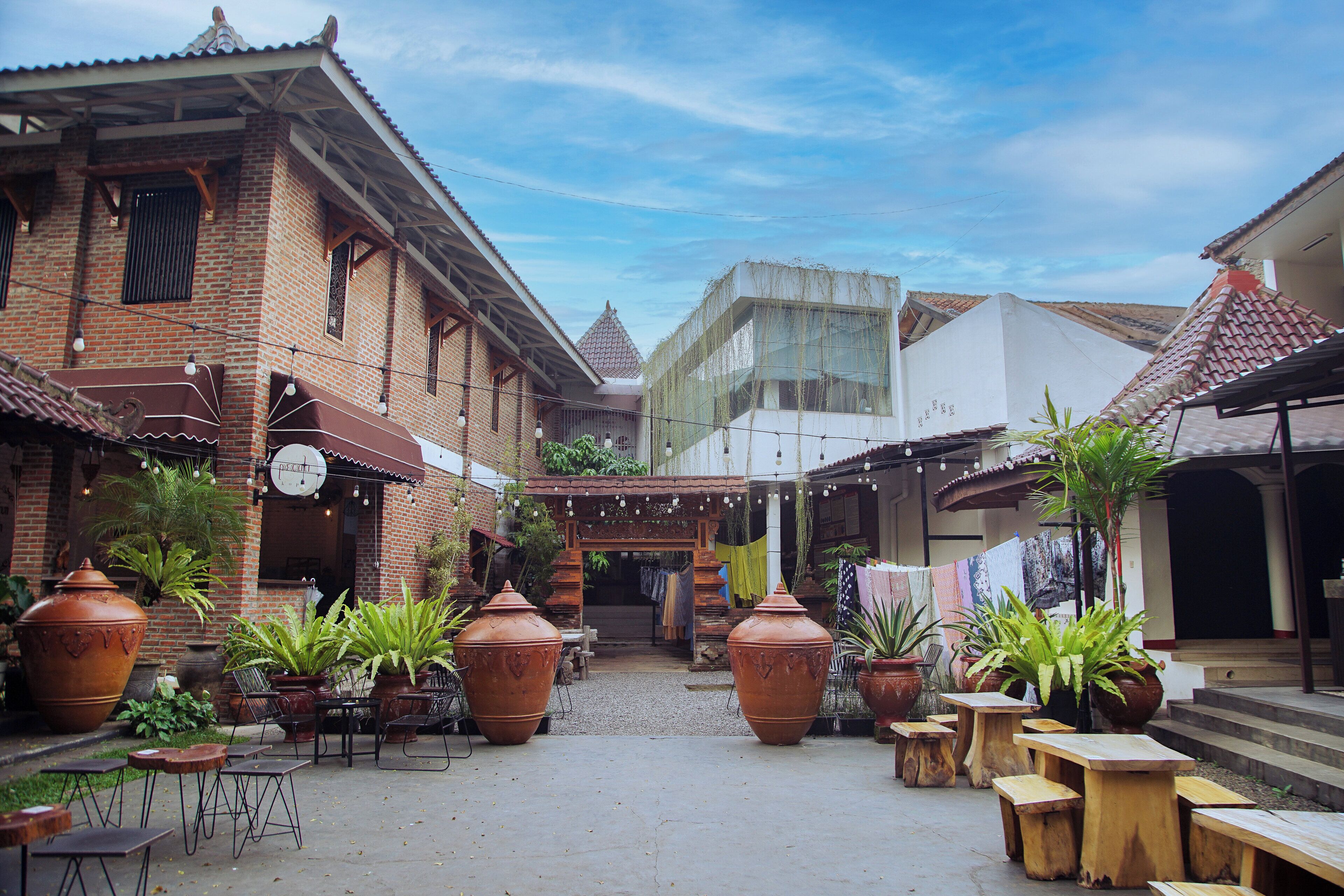 Un patio con edificios de ladrillo, grandes macetas de terracota, mesas y sillas de madera.