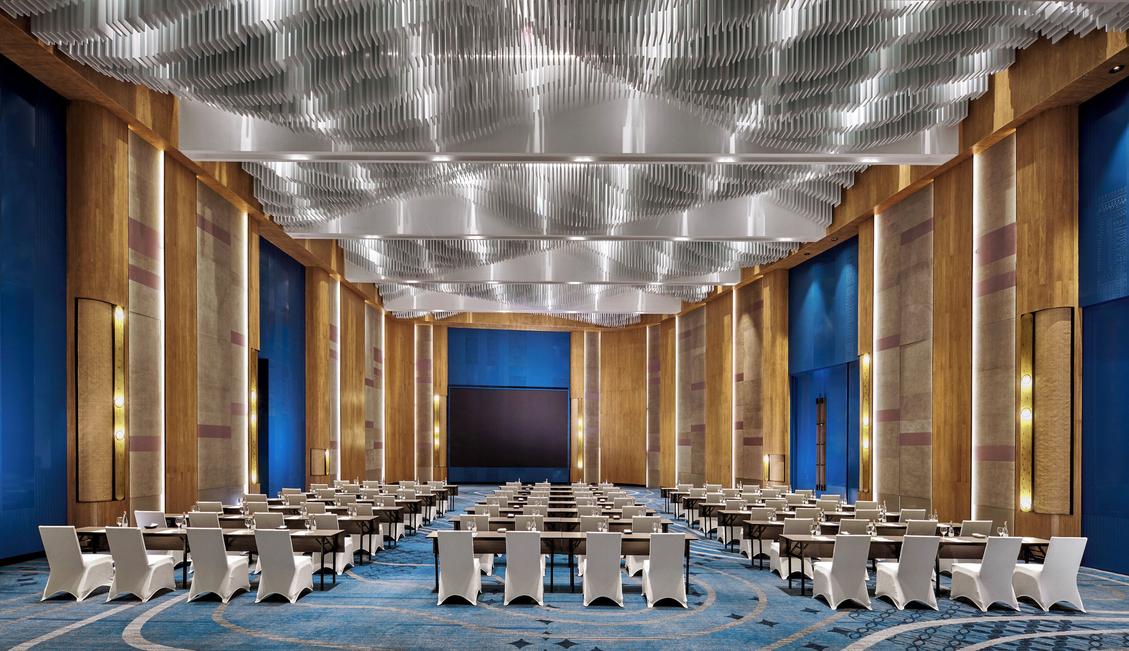 A conference room with rows of tables and chairs, a patterned carpet, and wooden paneling on the walls.