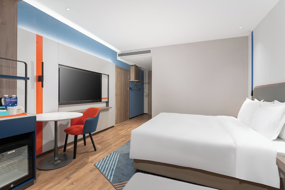 Een moderne hotelkamer met een groot bed, een flatscreen televisie, een bureau met stoel en een minibar.