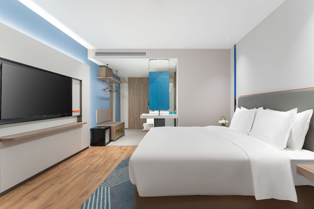 Een moderne hotelkamer met een groot bed, een flatscreen-televisie, een badkamer met spiegel en een houten vloer.