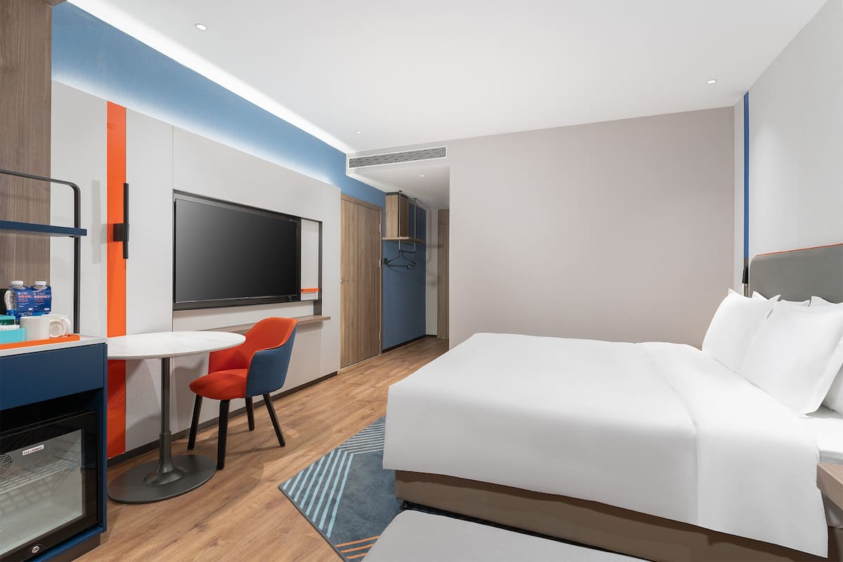 Een moderne hotelkamer met een groot bed, een flatscreen televisie, een bureau met stoel en een minibar.