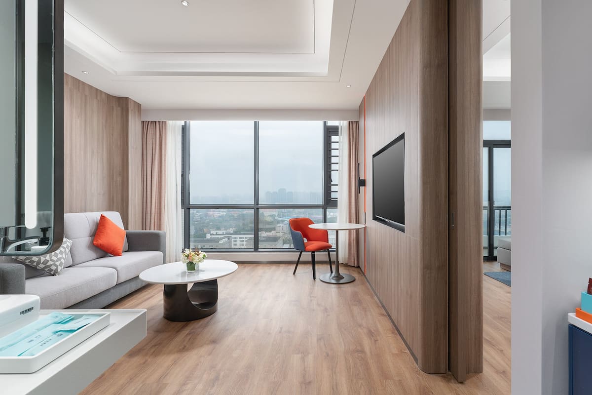 Een moderne woonkamer met een bank, een salontafel, een televisie en een groot raam met uitzicht op de stad.
