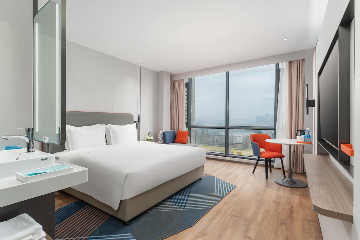 Een moderne hotelkamer met een groot bed, een bureau, een stoel, een televisie en een badkamer met een wastafel en spiegel.
