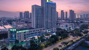 Un grand hôtel à plusieurs étages, avec une enseigne bien visible au sommet, situé dans un quartier urbain entouré d’autres immeubles et traversé par une route.