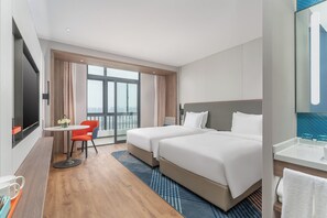Ett hotellrum med två sängar, ett litet bord med en stol, en TV och ett stort fönster.
