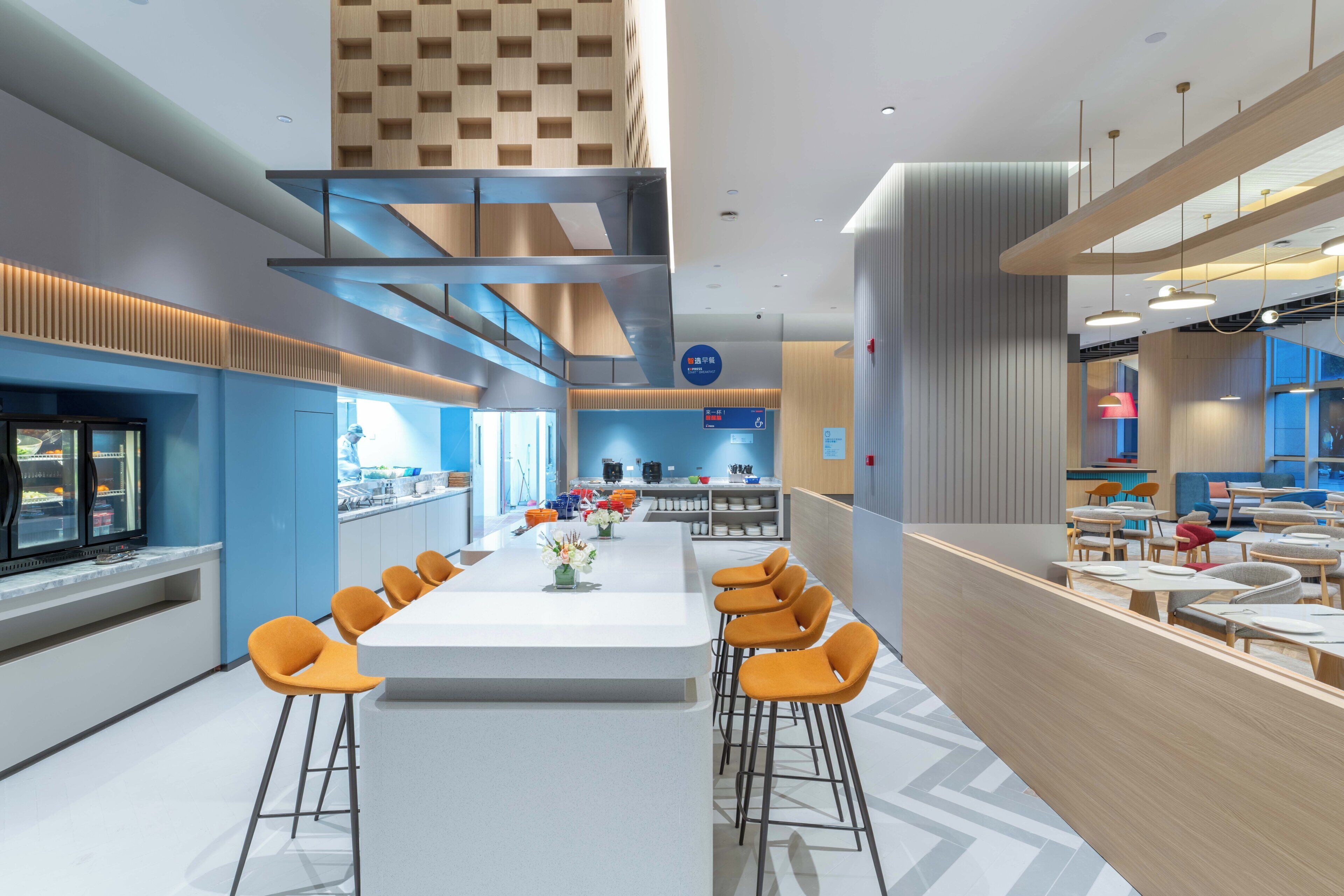 Un espace repas moderne avec une longue table, des tabourets de bar et une cuisine en arrière-plan.