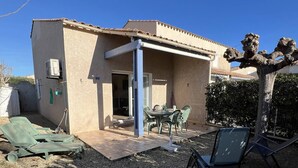 A house with a covered patio, outdoor furniture, and a tree. - Nice 3 room villa pool Rochelongue Cap d'Agde (LE CAP D AGDE)