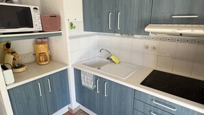 A compact kitchen with blue cabinets, a white countertop, a microwave, a coffee maker, and a sink. - Nice 3 room villa pool Rochelongue Cap d'Agde (LE CAP D AGDE)
