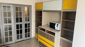 A room with a sliding glass door closet, a microwave on a wooden shelf, and a small table with a bottle. - Apto DE Luxo Standard 2 Quartos EM Caldas Novas (Olegário Pinto Caldas Novas)