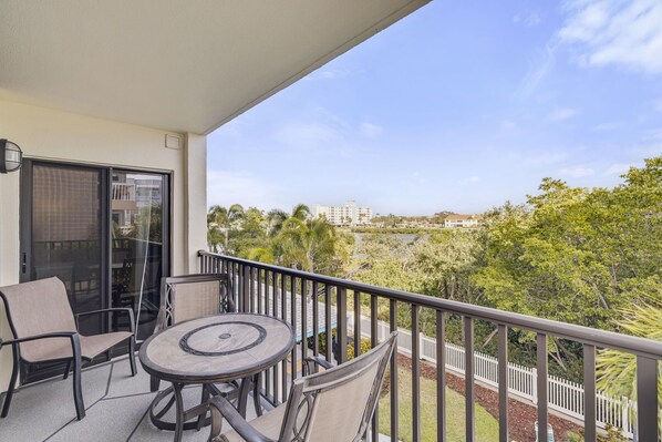 A balcony with a table and chairs, a glass door, and a view of a cityscape and greenery.
