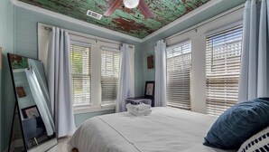 Un dormitorio con cama, ventilador de techo y ventana con persianas.
