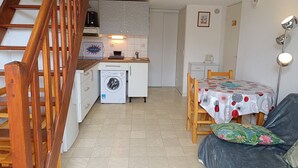 Eine kleine Küche mit Waschmaschine, eine Essecke mit Tisch und Stühlen sowie eine Treppe.